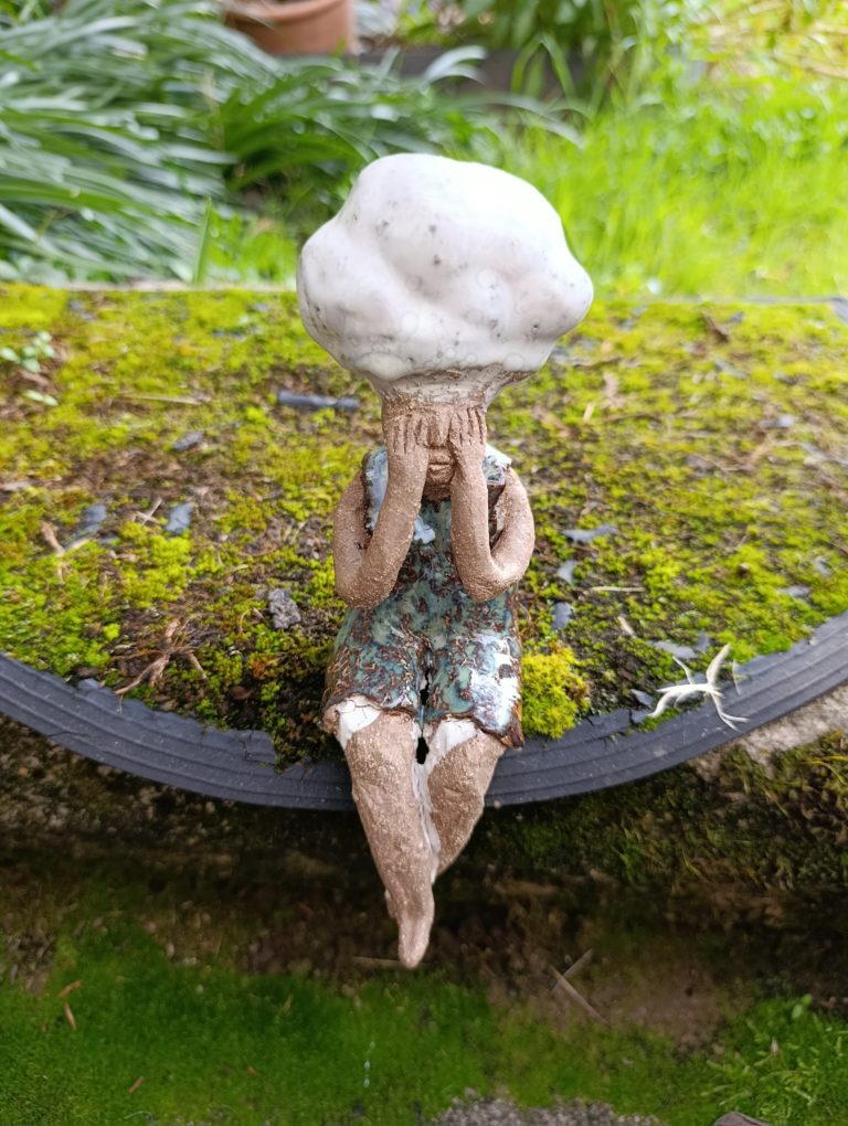 Sculpture en grès qui représente un personnage féminin se cachant les yeux et surmonté d'un nuage